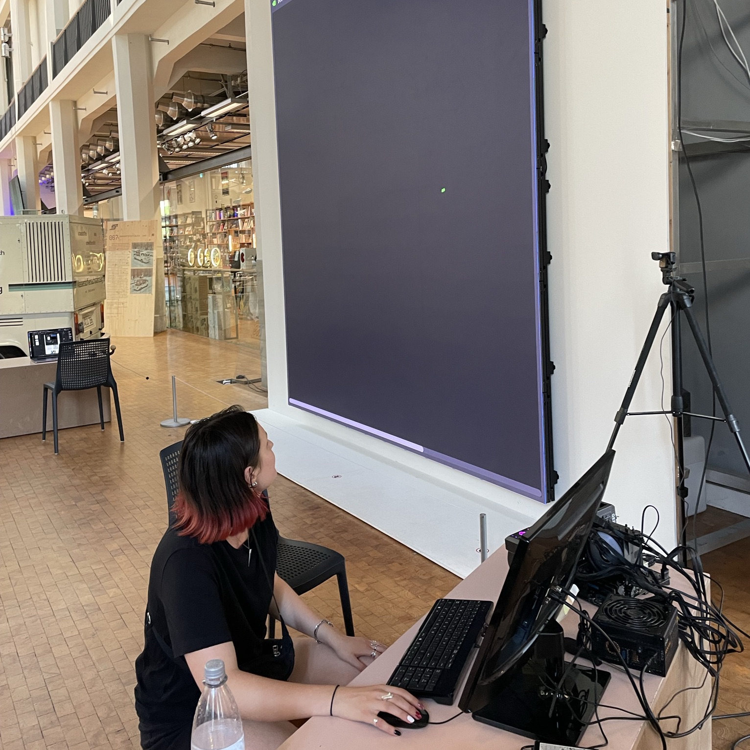 Eine Frau sitzt vor einem Wandgroßen LED Bildschirm und drückt Tasten auf einer Tastertur.