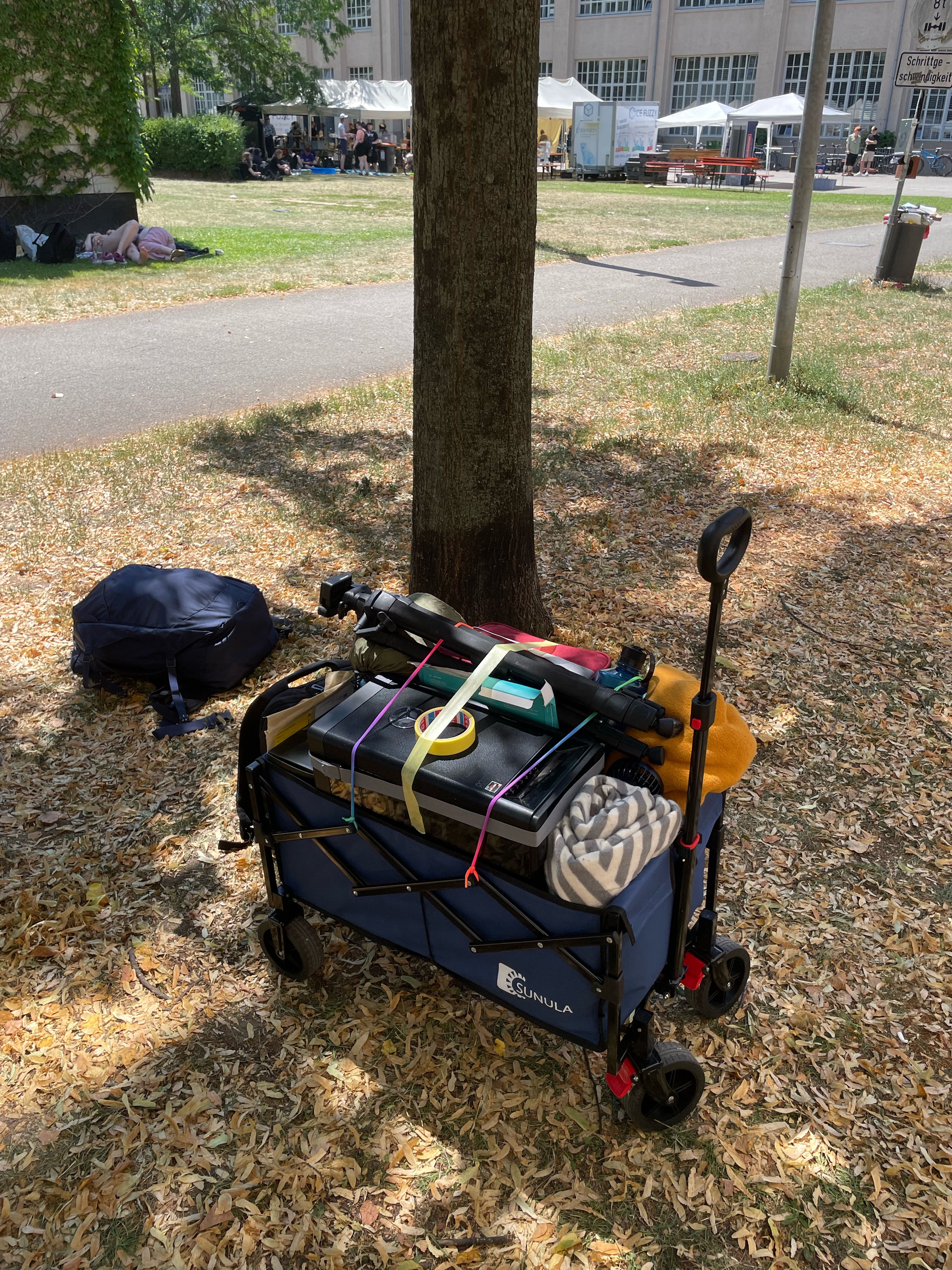 Ein vollgepackter Handwagen steht auf einer Wiese und wartet auf seinen Abtransport. Er ist vollgepackt mit Decken, Technik, Stativen und Rucksäcken.