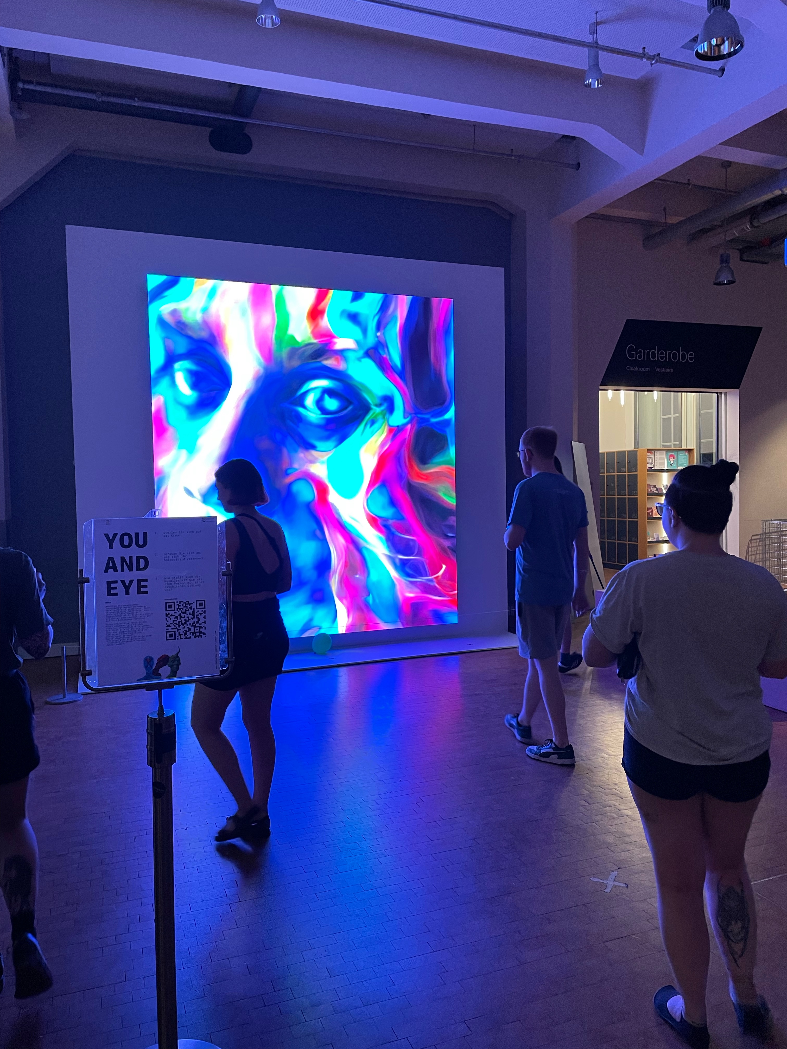 Auf dem LED Bildschirm ist ein buntes Gesicht in vielen Farben zu erkennen. Vor dem LED Bildschirm laufen drei Personen und verändern so, was auf dem LED Bildschirm angezeigt wird.