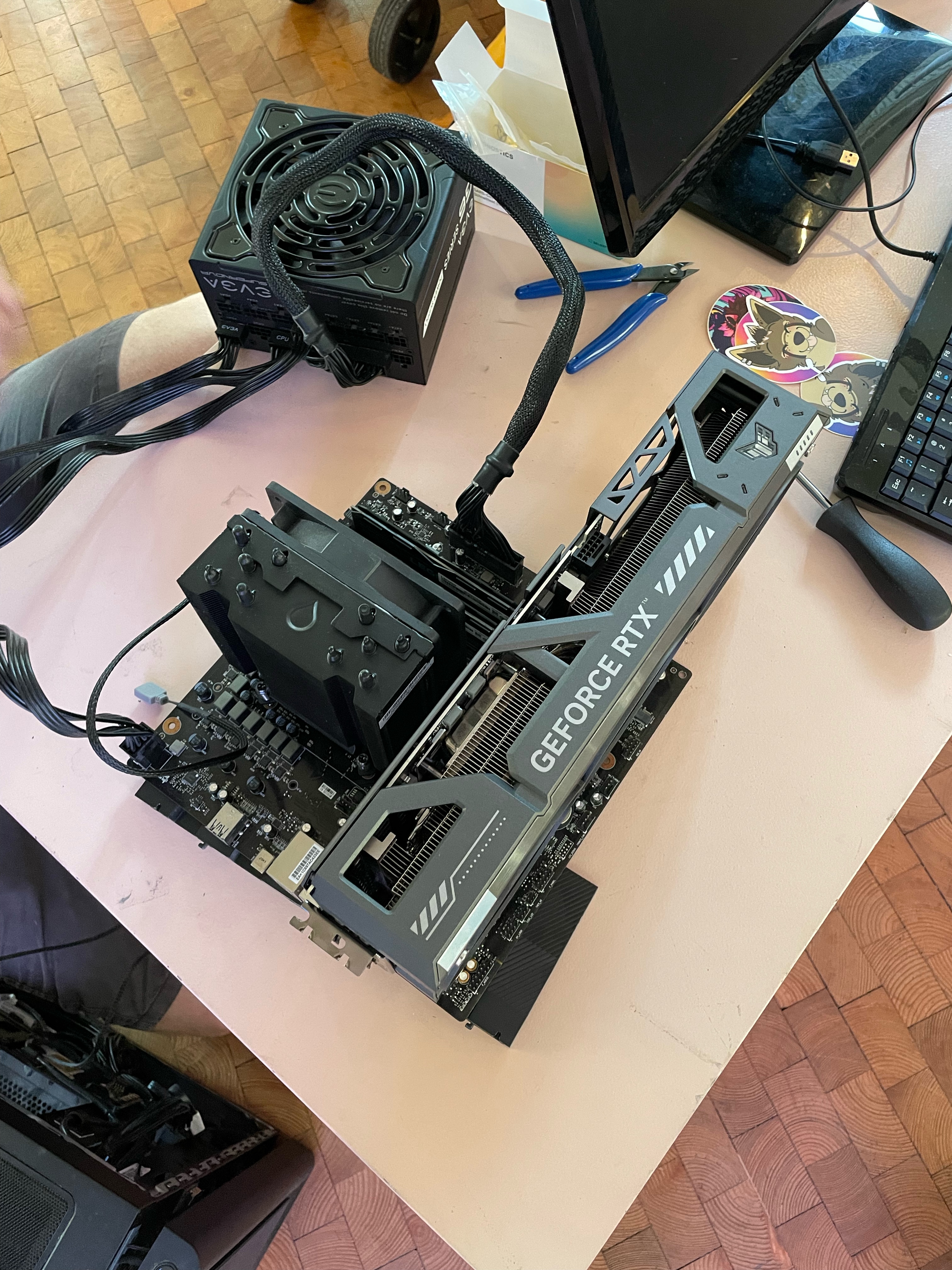 Auf einem ausgebauten Motherboard balanciert die Grafikkarte und ihre Extra-Lüfter. Das Netzteil ist ebenfalls ausgebaut und angeschlossen.