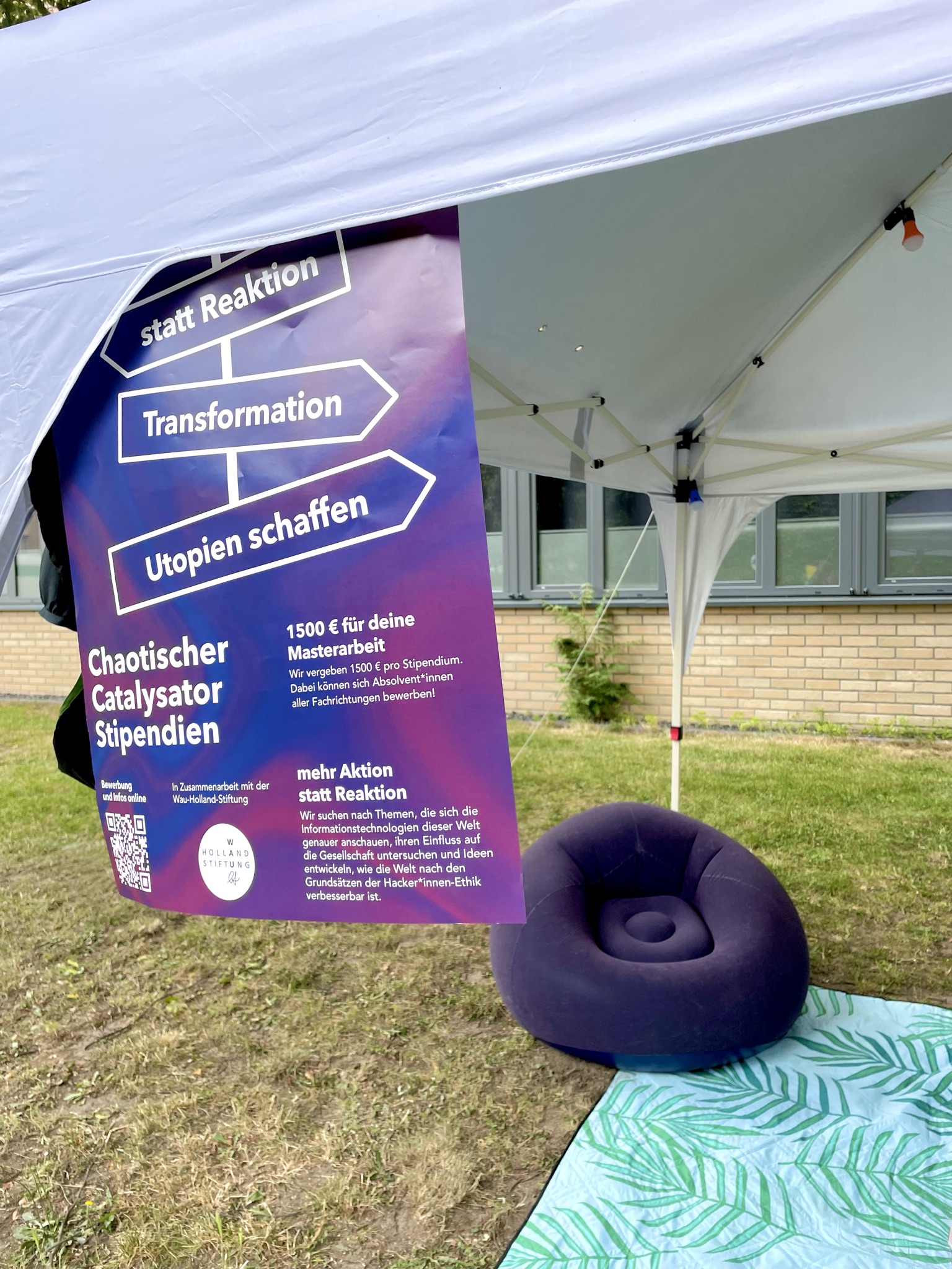 Blick unter einen weißen Garten-Pavillion. Am Pavillion Dach hängt ein CCS Werbeposter. Unter dem Pavillion steht ein dunkel blauer Outdoor-Sessel.