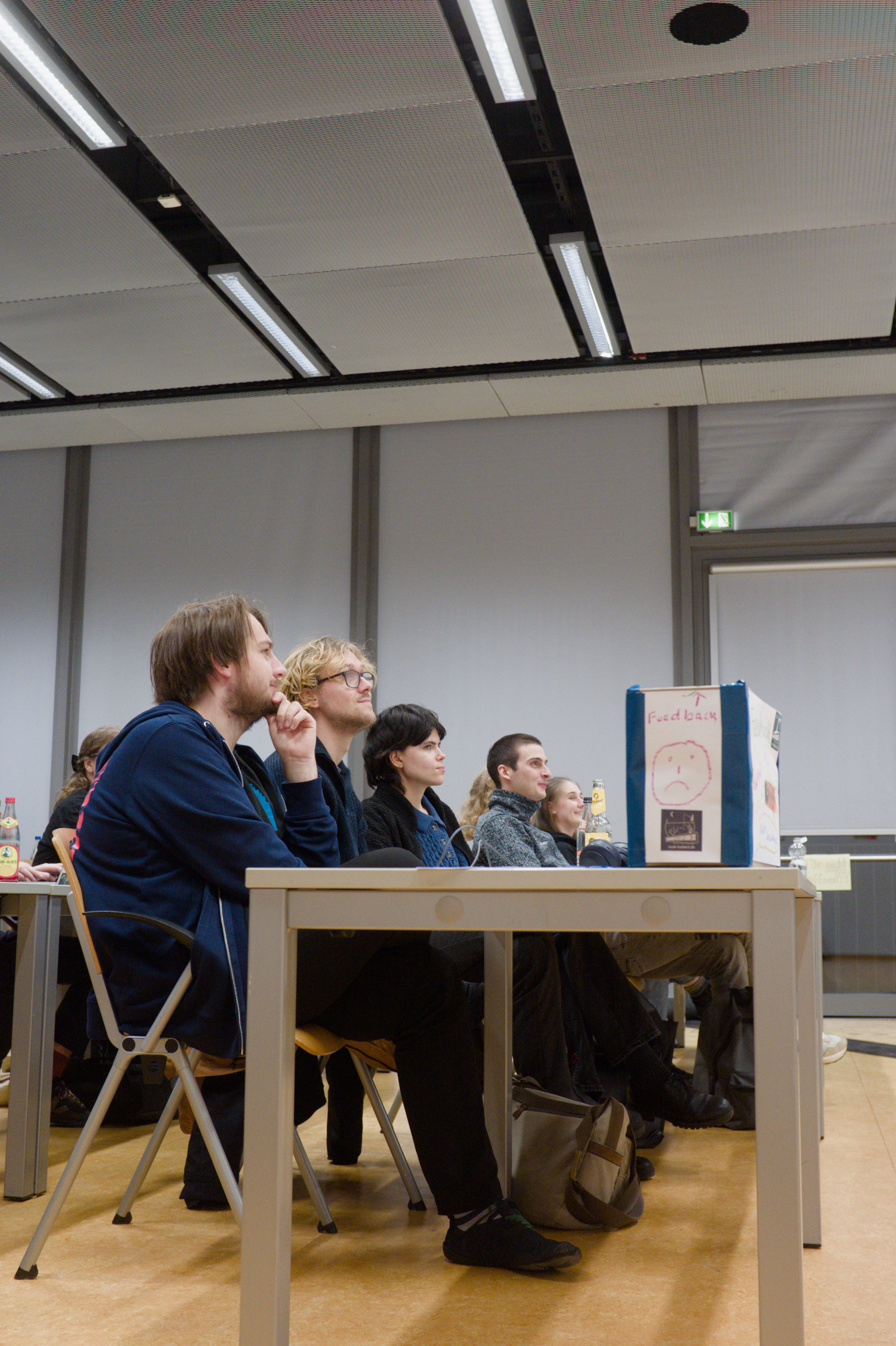 Fünf Personen sitzen auf Stühlen und folgen gespannt einem Vortrag, welcher selbst nicht zu sehen ist.