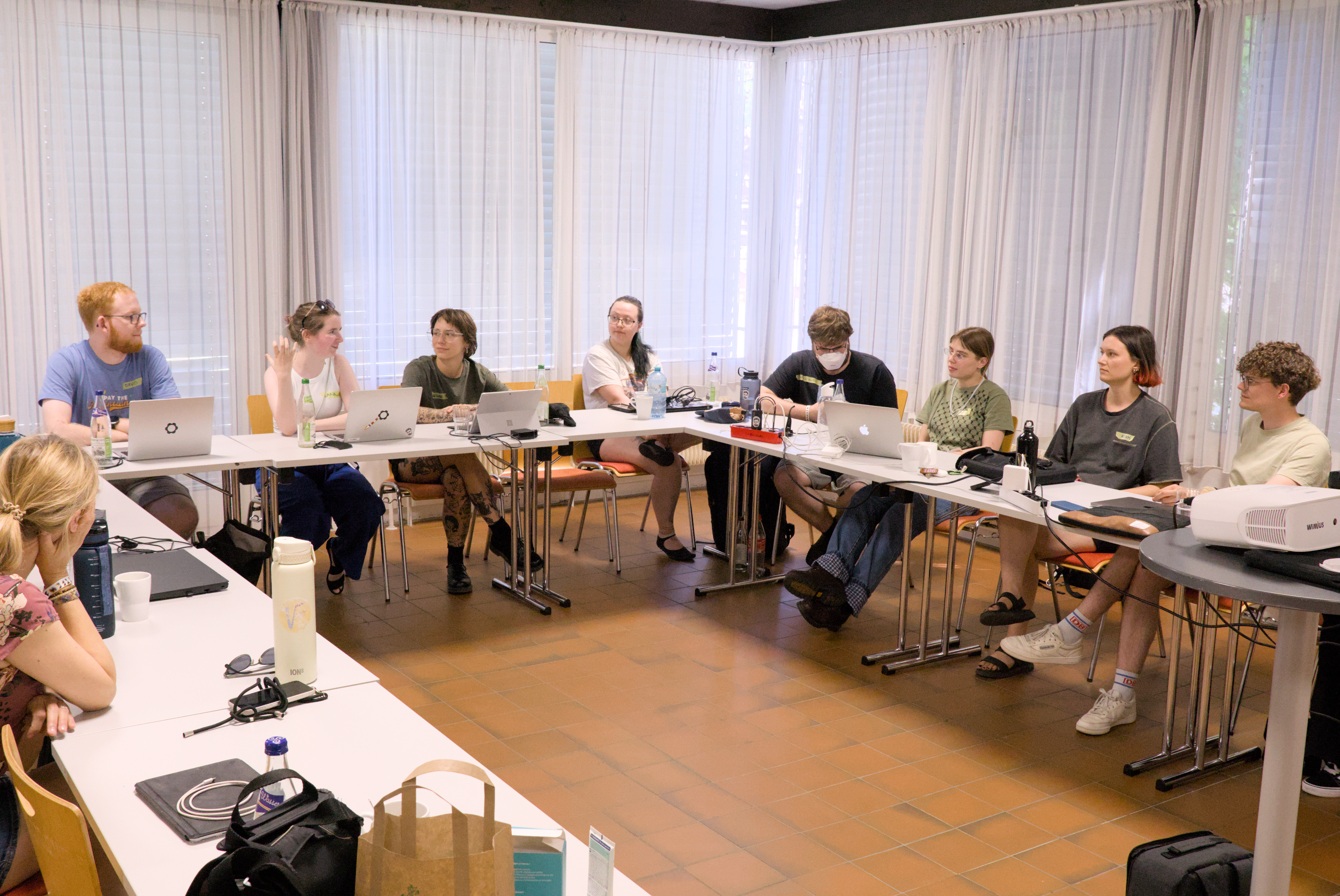 Eine Person in der Mitte der Tisch-Gruppe spricht. Die anderen Teilnehmenden hören zu.